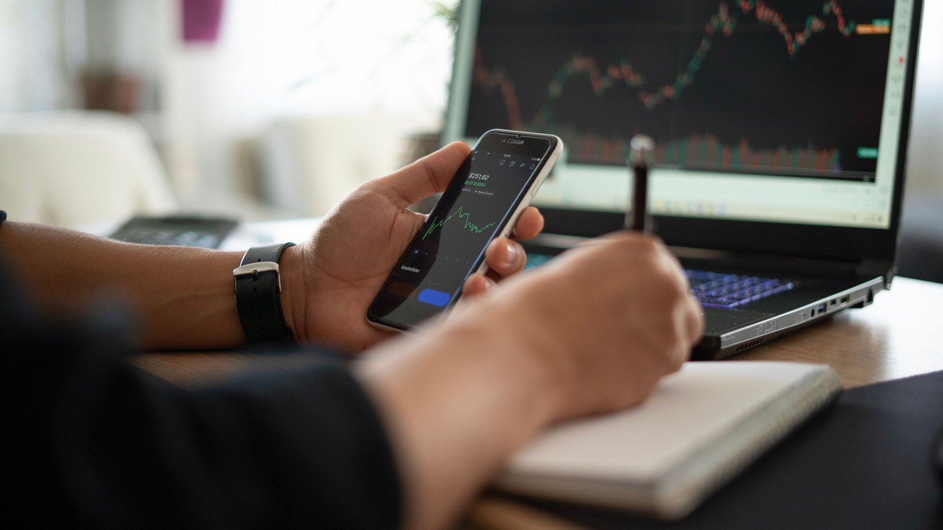 Businessman follows stock market on laptop and phone and takes notes